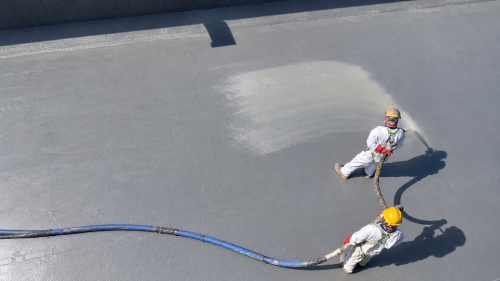 Technicians applying a polyurea waterproofing membrane to a concrete roof